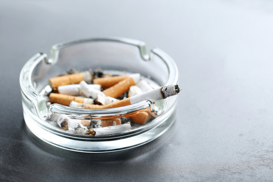Cigarette butts with ash in ashtray on black background