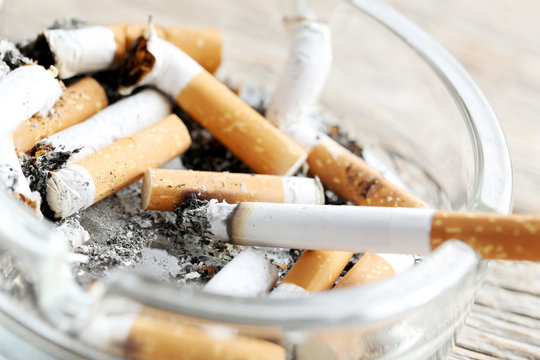 Cigarette butts with ash in ashtray on grey wooden table