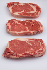 Three Ribeye steaks on a white cutting board
