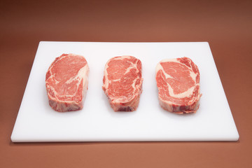 Three Ribeye steaks on a white cutting board