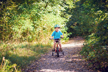 Obraz premium Child riding a bicycle. Kid in a helmet riding a bike in the forest. Beautiful baby. Toned image.