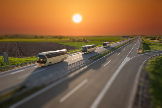Tilt shift image of fast travel buses on the highway at sunset