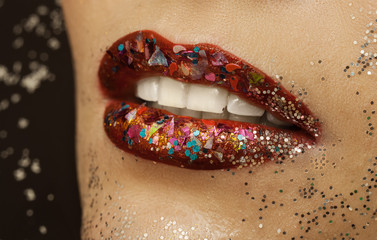 lips in red lipstick with multi-colored spangles of various form, a close up