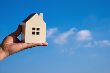 hand holding a house model and a blue sky at background