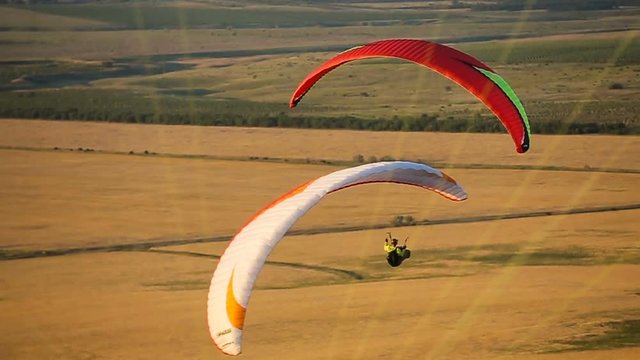 Flying paraglider over the field in a mountainous area at sunset on a summer day.Flying parachute over fields rolling hills.
