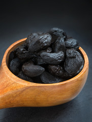Organic black Garlic, Macro selective focus shot of fresh organic black garlic cloves in a rich colored wooden spoon on grey slate. room for copy space and text © freila