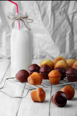 chocolate and simple mini muffins on white wooden table scattered.Selective focus.Three muffins on first plan many muffins and bottle of milk with tubule on second plan.
