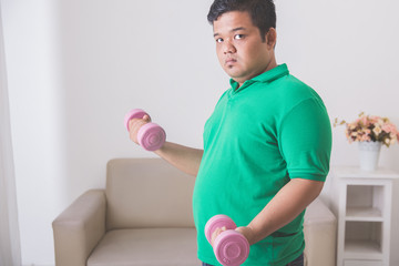 overweight man doing exercise at home, lifting up a dumbbell at