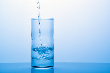 Pouring drinking water into the glass with reflection