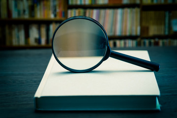 Magnifying glass on books with background of bookshelf