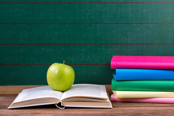 Apple and colored books on the chalkboard background