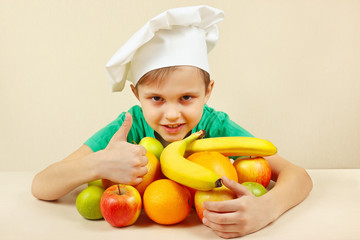 Little boy in chefs hat with fruits at the table