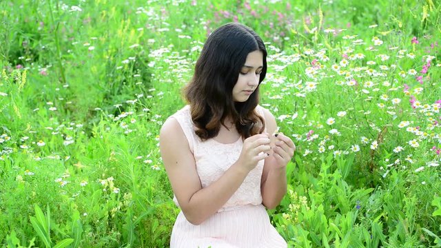 Young girl guesses on camomile in a meadow