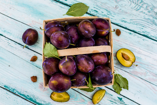 Ripe plums in a basket on a wooden table.
