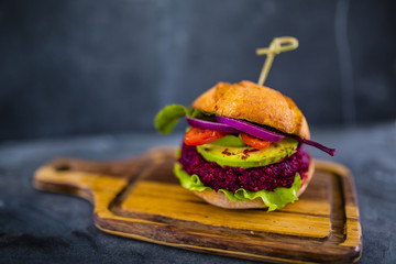 Tasty street food grilled vegetarian beetroot burger in crispy bun with lettuce and avocado served on small cutting board.