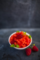 Granita of frozen watermelon with raspberries and lemon balm on dark stone background with space for text.