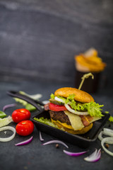 Tasty street food grilled beef burger in crispy shortbread with lettuce and fresh vegetables on stone dark background.