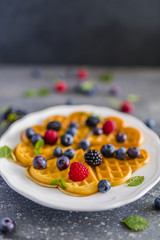 Homemade Belgian waffles with fresh ripe berries served on white plate.
