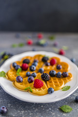 Homemade Belgian waffles with fresh ripe berries served on white plate.
