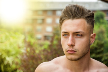 Headshot of handsome shirtless young man outdoor, looking away