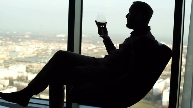 Silhouette of man relaxing and drinking wine while sitting on armchair at home 
