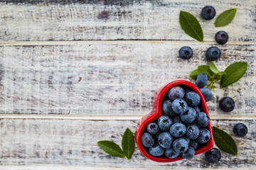 Fresh blueberries in a bowl in the shape of a heart on a wooden background. Space for text.