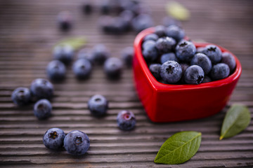 Fresh blueberries in a bowl in the shape of a heart on stone background