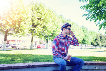 Fototapeta premium man in shirt and jeans glasses, talking on the phone, smartphone, the concept of summer, businessman vacation. City lifestyle. the street in the park.