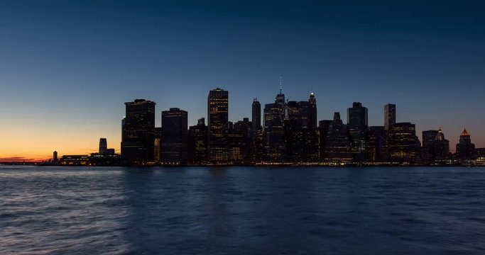 Time lapse cityscape view of the New York City Financial District and East River with passing boats. Lower Manhattan skyscrapers between sunset and dusk with city lights