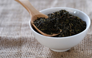 Tea on wooden spoon in white cup with sackcloth floor.