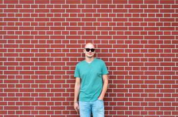 The bald man in sunglasses against the background of a red brick wall