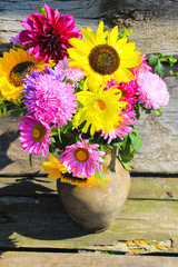 Autumn flowers in rustic clay jug on wooden background