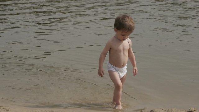 baby boy wearing swimming shorts playing on a beach. Slow motion