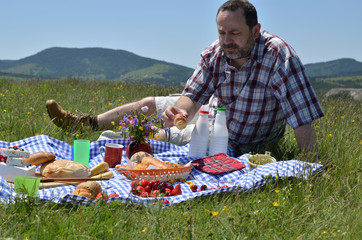 Obraz premium Man on picnic is taking a bun and preparing to eat it, on sunny day