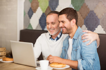 Cheerful man and his adult grandson resting in the cafe
