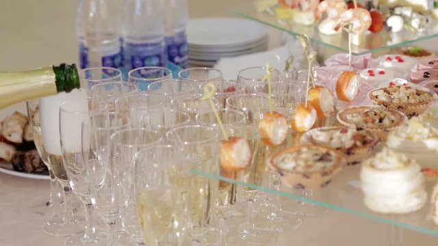 Банкетный стол с закусками, официант наливает шампанское в фужеры. Кейтеринг