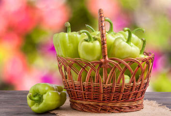 green bell peppers in a wicker basket on  wooden table with  blurred background