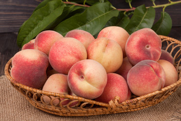 peaches in a wicker basket with leaves on wooden table