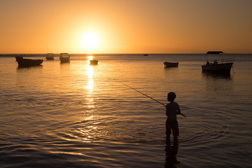 Enfant pêchant les pieds dans l'eau à l'île Maurice face au coucher de soleil