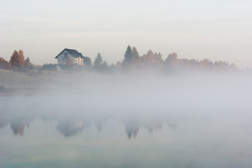 Early morning on the lake in the autumn, the silhouette of house on the shore.
