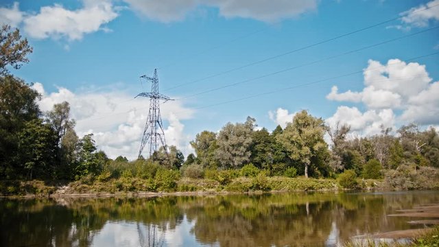 Wide shot timelapse of electricity power lines and high voltage pylons on a field in the countryside at summer near river