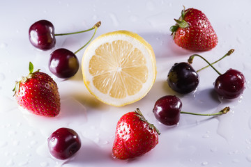 Washed lemon, cherries and strawberries with drops of water on w