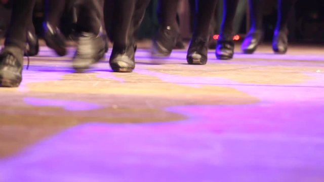 Two rows of people doing Irish dance with traditional step shoes. Close up double line of female dancing feet on stage became one. Music, tradition and culture of Ireland. Celtic show on wooden floor