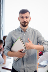 Portrait of handsome businessman showing thumb-up while holding clipboard in office interior. Bearded man looking at camera. Business or freelance concept.