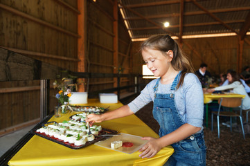 Little girl serving herself fresh cow cheese, healthy snack, farm style party