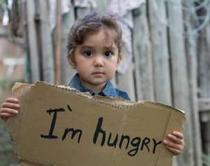Little girl holding a sheet of cardboard. On the cardboard label "I am hungry." The child is three years.

