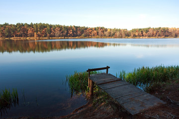 Old small wooden pier for fishing in autumn forest lake