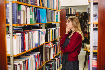 Pensive girl chosing a book in college library. Education concept
