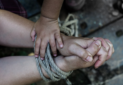Thick rope ties the hands of women. Child's hand holding a rope.
