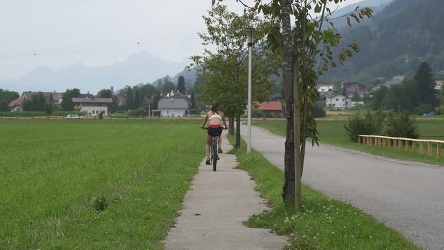 Fit woman cycles along the bike trail near green field in village
